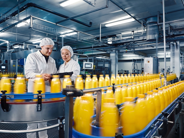 Två ingenjörer på en anläggning för dryckestillverkning övervakar påfyllningsprocessen för apelsinjuice.